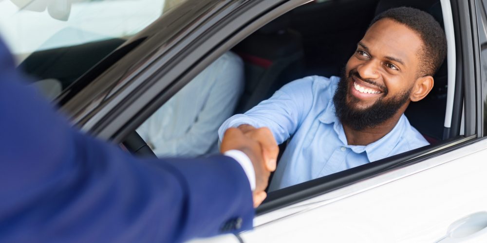 Black Male Customer Sitting Inside Of His New Car And Shaking Hands With Salesman After Buying Own Automobile In Modern Dealership Center, Salesperson Greeting Happy African American Man, Closeup