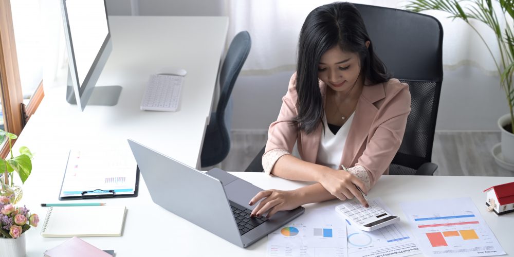 Female professional accountant using calculator and preparing annual financial report at workplace.